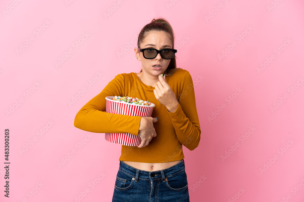 Young Lithuanian woman isolated on pink background with 3d glasses and holding a big bucket of popcorns Young Lithuanian woman isolated on pink background with 3d glasses and holding a big bucket of popcorns