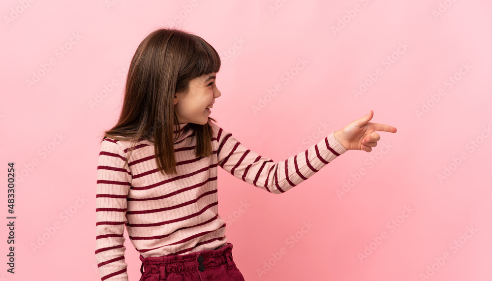 Little girl isolated on pink background pointing finger to the side and presenting a product Little girl isolated on pink background pointing finger to the side and presenting a product