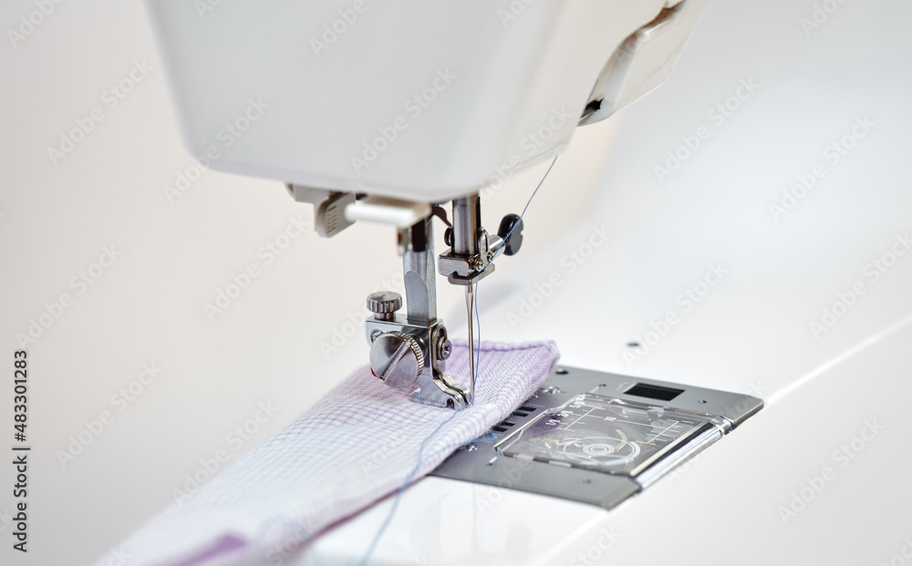 Sewing machine working part with violet cloth, replacement foot. A close-up shows a needle passing through tissue. Sewing machine with fabric and thread