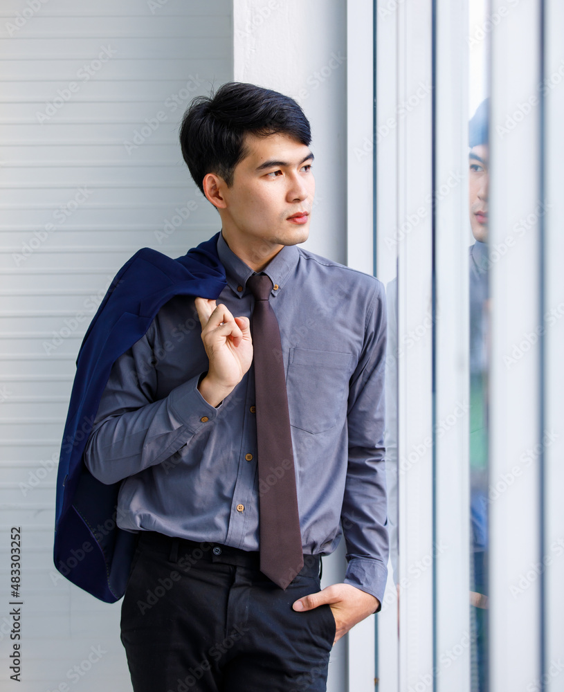 Portrait studio shot of millennial Asian confident professional successful male manager businessman entrepreneur in formal outfit standing smiling holding suit jacket standing near skyscraper Portrait studio shot of millennial Asian confident professional successful male manager businessman entrepreneur in formal outfit standing smiling holding suit jacket standing near skyscraper