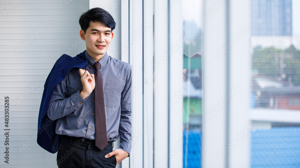 Portrait tudio shot of millennial Asian confident professional successful male manager businessman entrepreneur in formal outfit standing smiling holding suit jacket standing near skyscraper office Portrait tudio shot of millennial Asian confident professional successful male manager businessman entrepreneur in formal outfit standing smiling holding suit jacket standing near skyscraper office