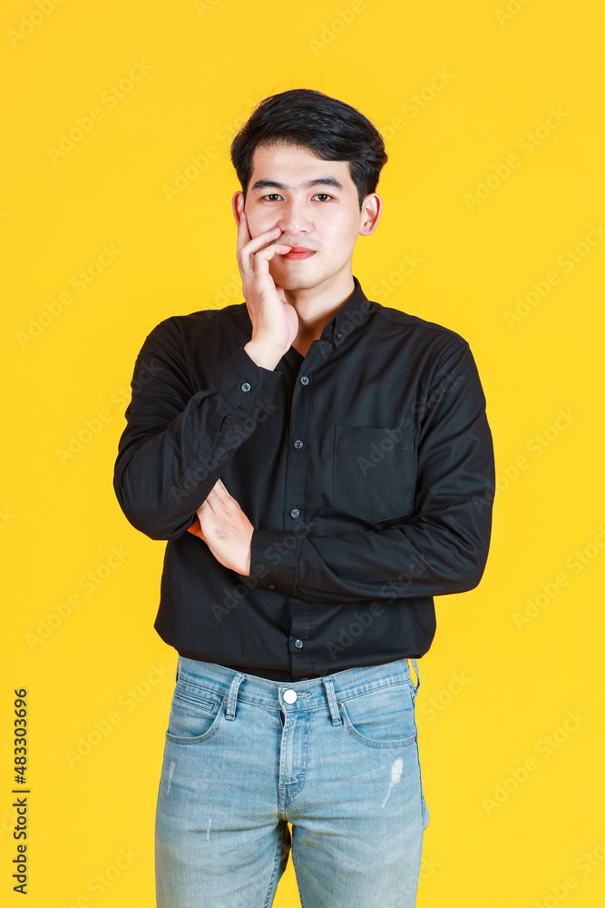 Portrait studio shot of Asian young man professional successful male businessman in casual black shirt standing smiling look at camera on yellow background Portrait studio shot of Asian young man professional successful male businessman in casual black shirt standing smiling look at camera on yellow background