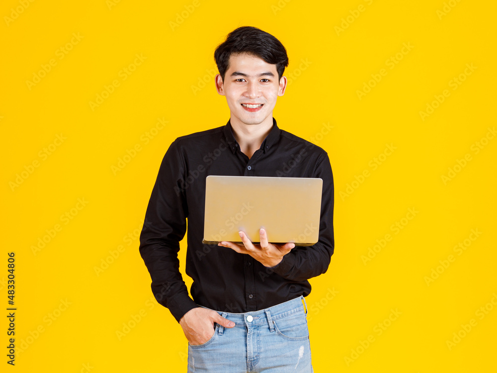 Portrait closeup studio shot of Asian man happy male businessman model in casual outfit standing holding laptop computer for advertising on yellow background Portrait closeup studio shot of Asian man happy male businessman model in casual outfit standing holding laptop computer for advertising on yellow background