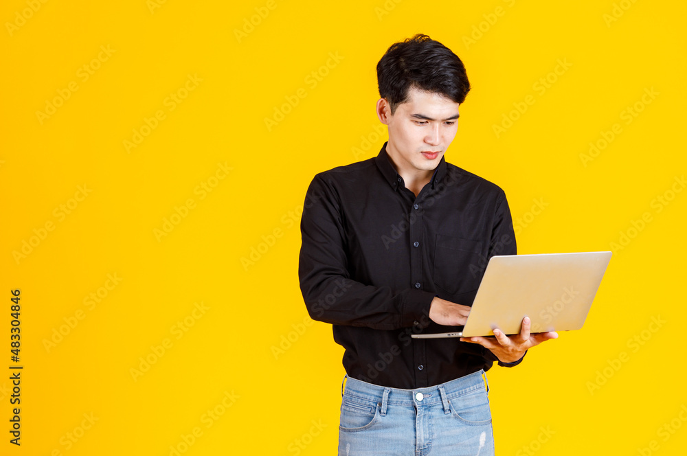 Portrait closeup studio shot of Asian man happy male businessman model in casual outfit standing holding laptop computer for advertising on yellow background