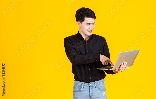 Portrait closeup studio shot of Asian man happy male businessman model in casual outfit standing holding laptop computer for advertising on yellow background