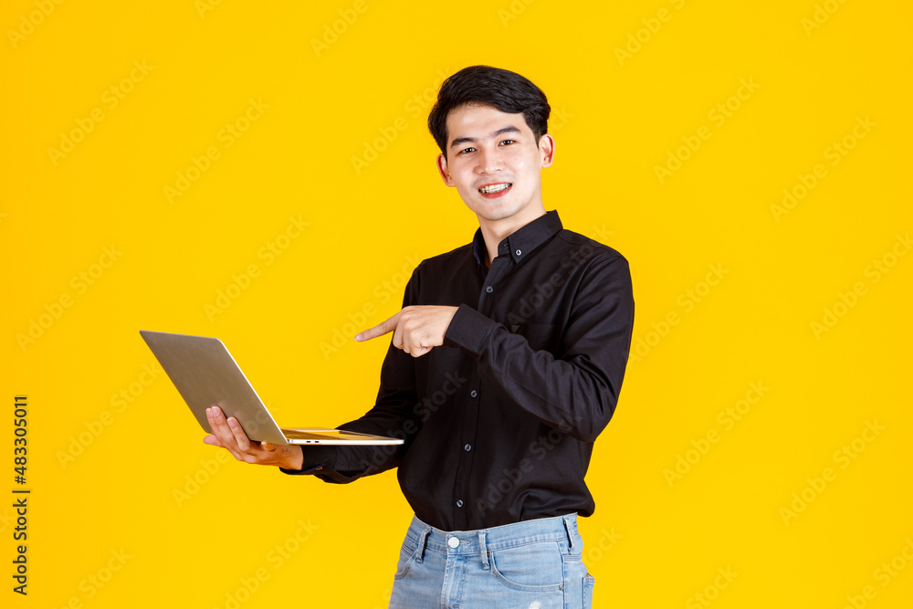 Portrait closeup studio shot of Asian man happy male businessman model in casual outfit standing holding laptop computer for advertising on yellow background