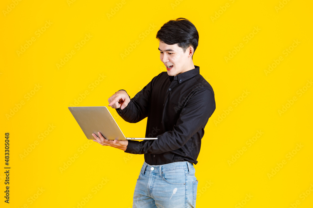 Portrait closeup studio shot of Asian man happy male businessman model in casual outfit standing holding laptop computer for advertising on yellow background Portrait closeup studio shot of Asian man happy male businessman model in casual outfit standing holding laptop computer for advertising on yellow background