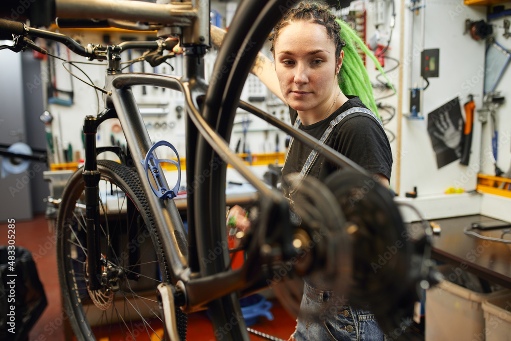 Obraz premium Female mechanic repairing bicycle in workshop