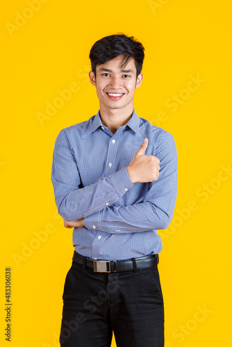 Portrait studio shot of millennial Asian young male professional successful businessman entrepreneur in formal shirt and slacks standing posing on yellow background.