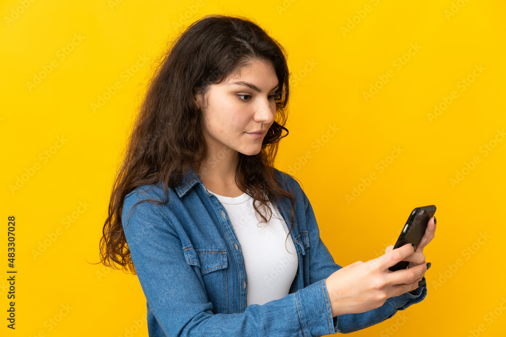 Teenager Russian girl isolated on yellow background sending a message or email with the mobile Teenager Russian girl isolated on yellow background sending a message or email with the mobile