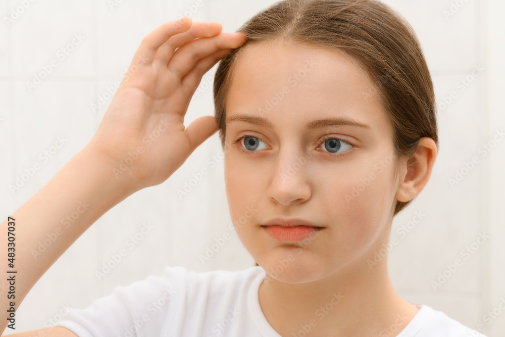 the face of a teenage girl, she looks at herself in the mirror and touches her face with her hand, good and clean skin is a concept of beauty and health the face of a teenage girl, she looks at herself in the mirror and touches her face with her hand, good and clean skin is a concept of beauty and health