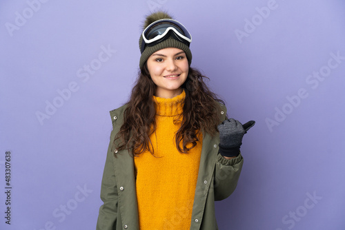 Teenager Russian girl with snowboarding glasses isolated on purple background pointing to the side to present a product