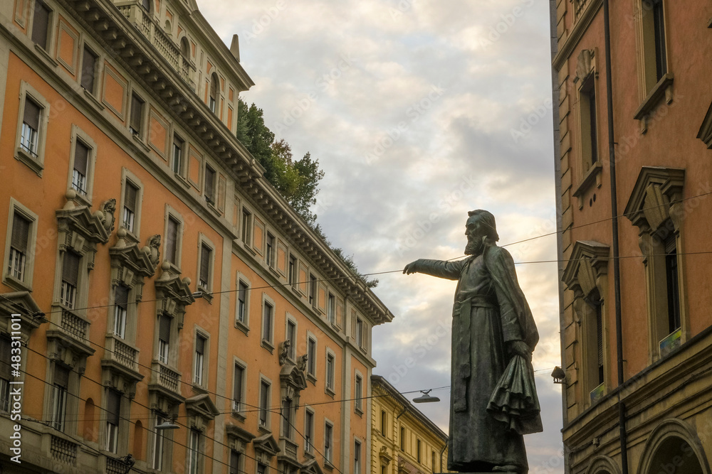 Naklejka premium the Statue of Ugo Bassi in the Ugo Bassi street across the orange buildings and sky in Bologna, Italy