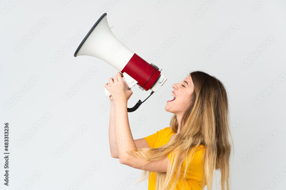 Young blonde woman isolated on white background shouting through a megaphone to announce something in lateral position Young blonde woman isolated on white background shouting through a megaphone to announce something in lateral position