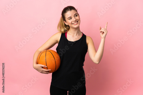 Young blonde woman playing basketball isolated on pink background pointing up a great idea