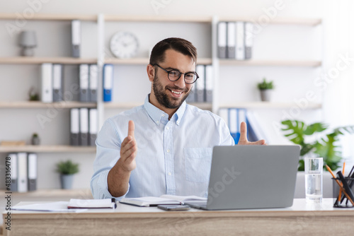 Happy mature caucasian guy with beard in glasses work at laptop, making video call and gesturing