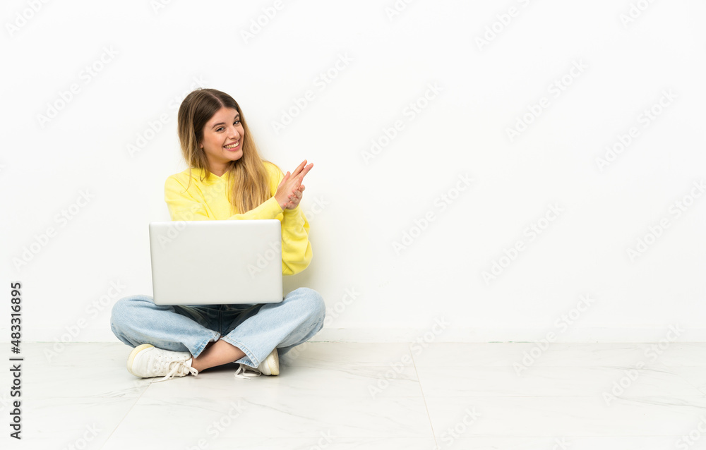 Young woman with a laptop sitting on the floor applauding Young woman with a laptop sitting on the floor applauding