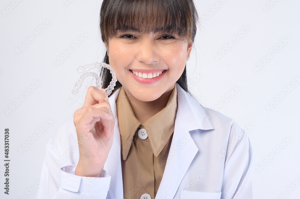 Young female dentist holding invisalign braces over white background studio, dental healthcare and Orthodontic concept. Young female dentist holding invisalign braces over white background studio, dental healthcare and Orthodontic concept.