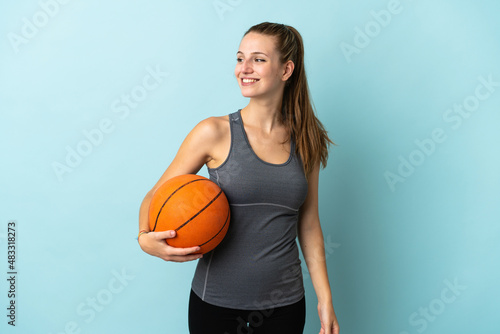 Young woman playing basketball isolated on blue background looking to the side and smiling