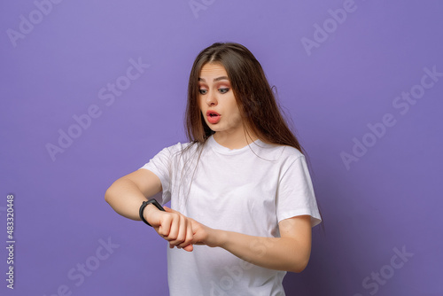 Too late, hurry up. Young beautiful brunette woman in hurry pointing finger on wrist watch, impatience, upset and angry for deadline delay. Studio shot, purple background