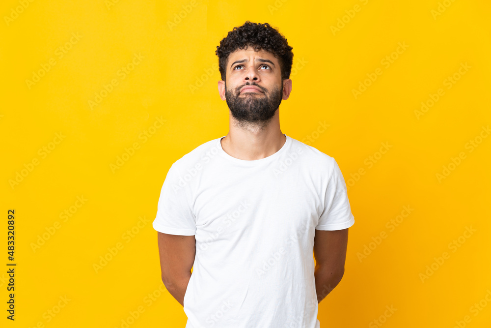 Young Moroccan man isolated on yellow background and looking up Young Moroccan man isolated on yellow background and looking up