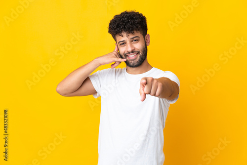 Young Moroccan man isolated on yellow background making phone gesture and pointing front