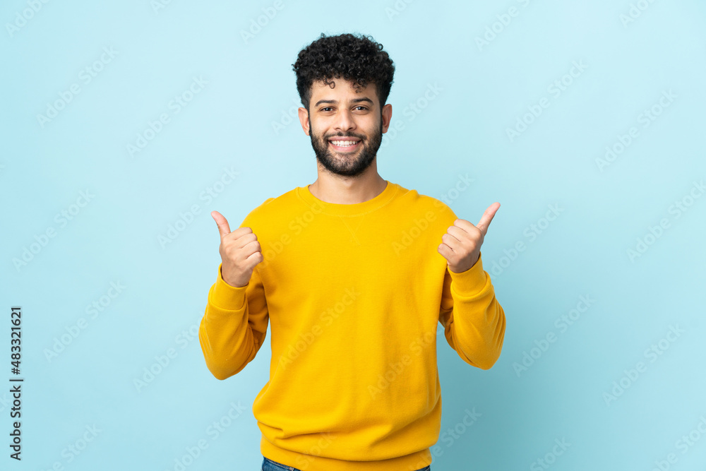 Young Moroccan man isolated on blue background with thumbs up gesture and smiling Young Moroccan man isolated on blue background with thumbs up gesture and smiling