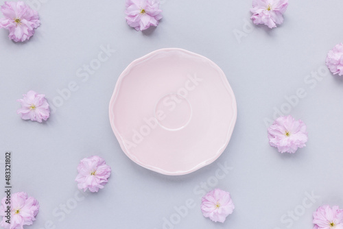 Empty small pink plate or saucer and fresh spring cherry blossom flowers on pastel gray background. Tea party, drinking coffee or dessert recipe concept. Top view, flat lay, copy space