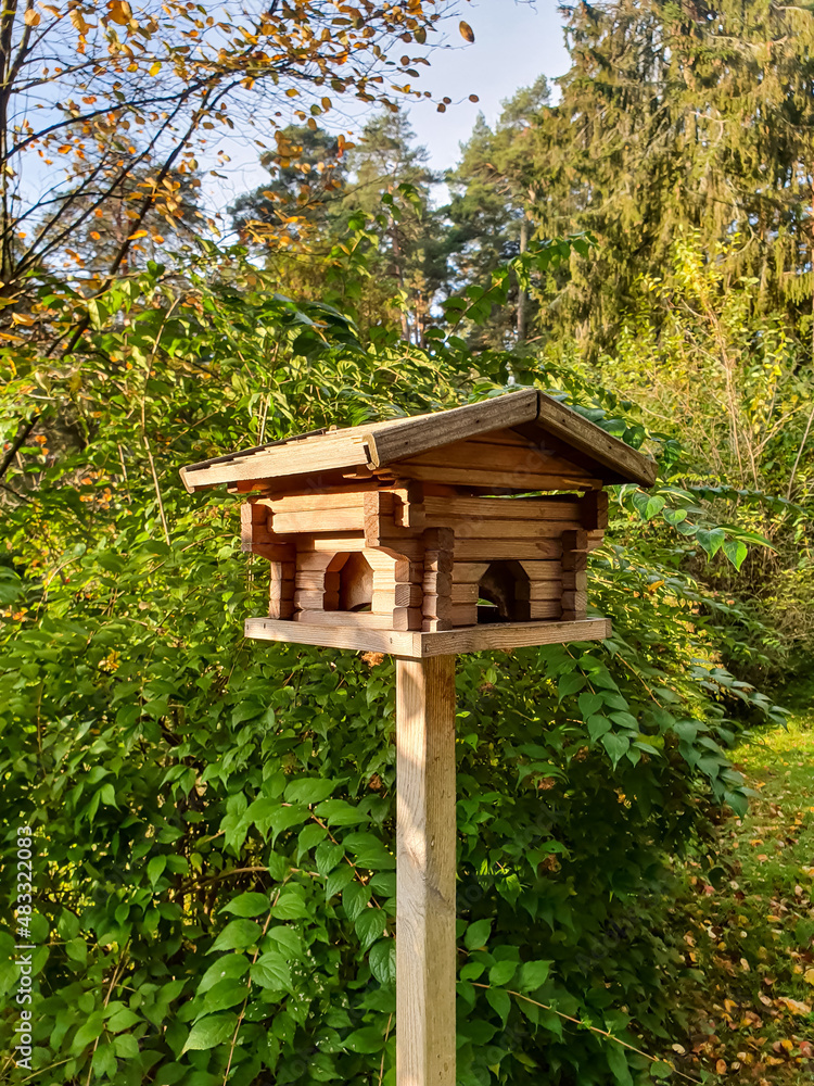 Wooden bird feeder in front of bushes Wooden bird feeder in front of bushes