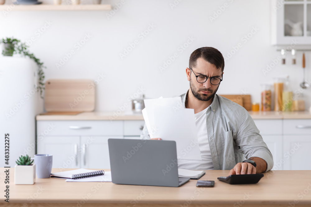 Busy adult caucasian man with beard in glasses counts finances, pays bill and taxes for calculator