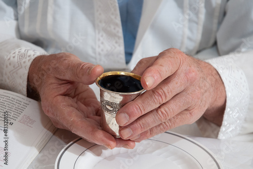 A man holds a silver cup and recites the blessing over wine during a Passover seder. 