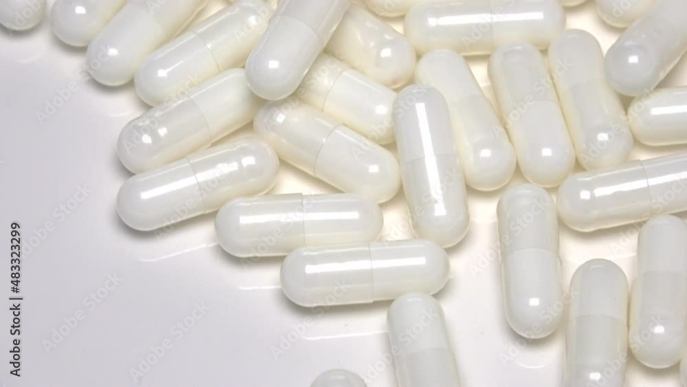 Closeup of many white medical capsules falling down on a white plate. Medicine and dietary supplements. 4K Closeup of many white medical capsules falling down on a white plate. Medicine and dietary supplements. 4K