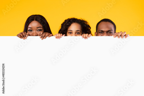 Black people peeking out blank white advertising billboard at studio photo