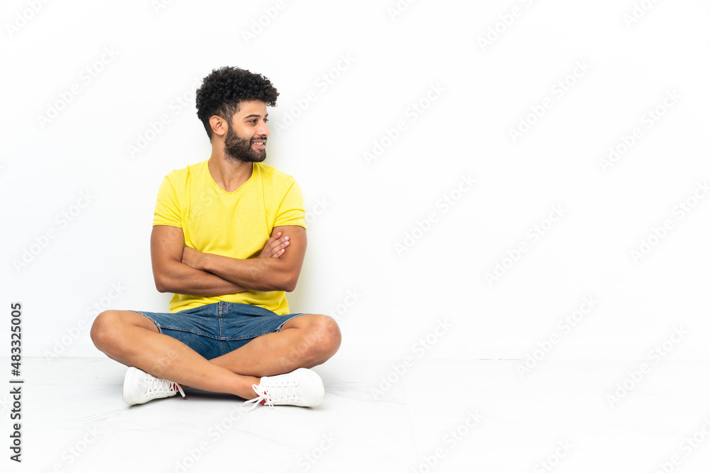 Fototapeta premium Young Moroccan handsome man sitting on the floor over isolated background looking side
