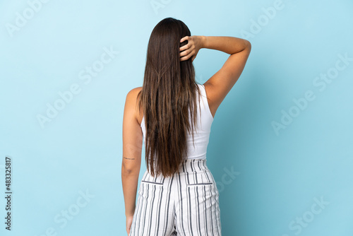 Young brazilian woman isolated on blue background in back position and thinking