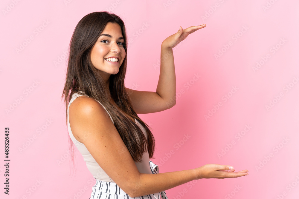 Young brazilian woman isolated on pink background holding copyspace to insert an ad Young brazilian woman isolated on pink background holding copyspace to insert an ad
