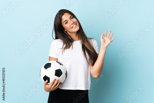 Young football player brazilian girl isolated on blue background saluting with hand with happy expression © luismolinero