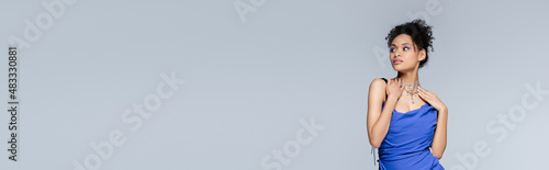 Fotografia curly young african american woman in bright blue dress isolated on grey, banner