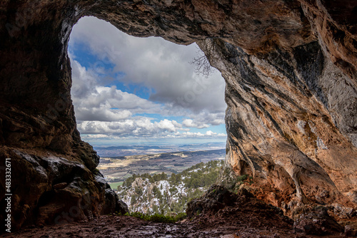 Bolumini cave from the inside, in the background a snowy landscape with blue sky. Mariola natural park ,Agres, Alicante, Spain.