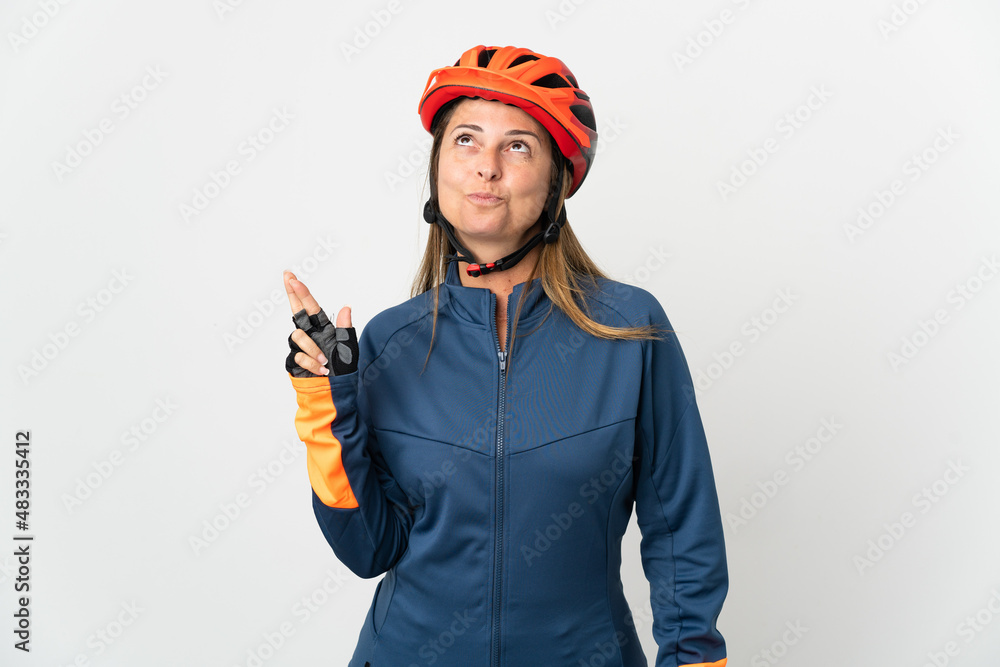 Middle age cyclist woman isolated on white background with fingers crossing and wishing the best Middle age cyclist woman isolated on white background with fingers crossing and wishing the best