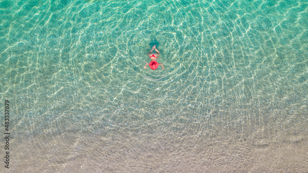 Top view. Young beautiful woman in a red hat and bikini swimming in sea water on the sand beach. Drone, copter photo. Summer vacation. View from above. Top view. Young beautiful woman in a red hat and bikini swimming in sea water on the sand beach. Drone, copter photo. Summer vacation. View from above.
