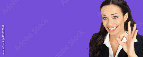 Portrait of businesswoman in black confident suit showing ok okay gesture, over violet purple colour background. Happy smiling brunette woman at studio. Business success concept.