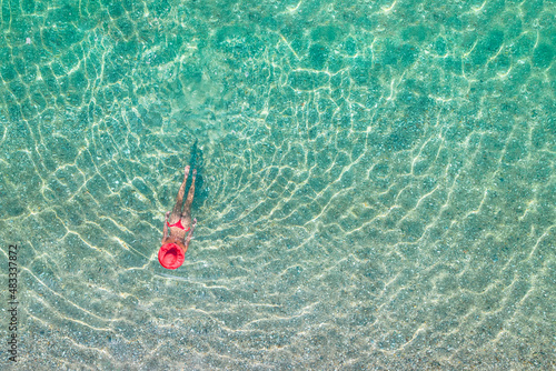 Top view. Young beautiful woman in a red hat and bikini swimming in sea water on the sand beach. Drone, copter photo. Summer vacation. View from above. © flowertiare