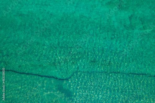 Background, texture of relaxing, calm turquoise, transparent sea water with stones, slabs, lump, coral. Summer vacation. Blue ocean lagoon. Drone, copter top view.