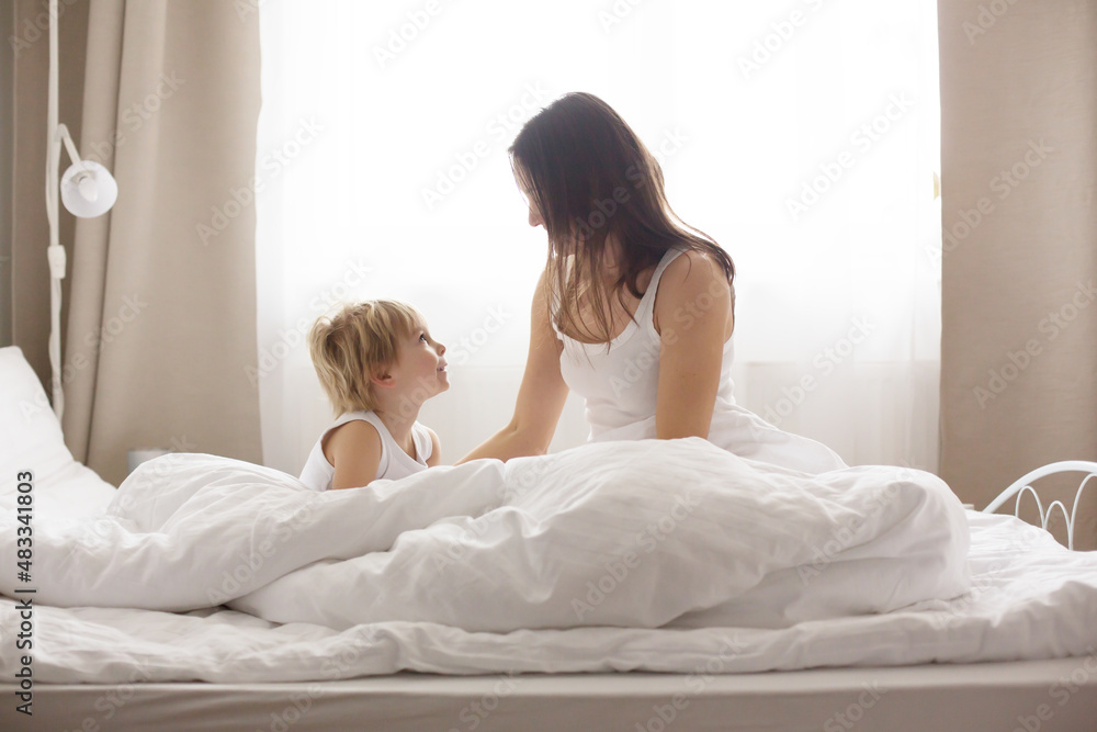 Beautiful blond child and his mother, playing at home in the morning in bed, smiling, laughing and having fun Beautiful blond child and his mother, playing at home in the morning in bed, smiling, laughing and having fun