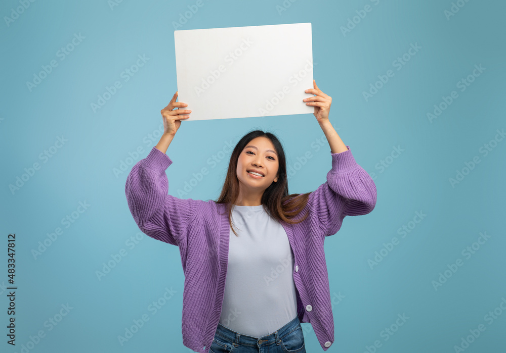 Advertisement concept. Happy asian lady holding empty white board and smiling at camera over blue background Advertisement concept. Happy asian lady holding empty white board and smiling at camera over blue background
