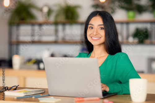 Positive millennial arabic lady looking for job online, cafe interior