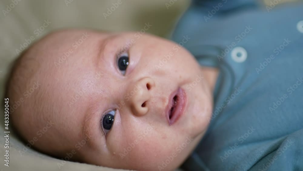 Adorable baby face portrait looking into camera. Sweet child lies on its back still at the grey background. Close up.
