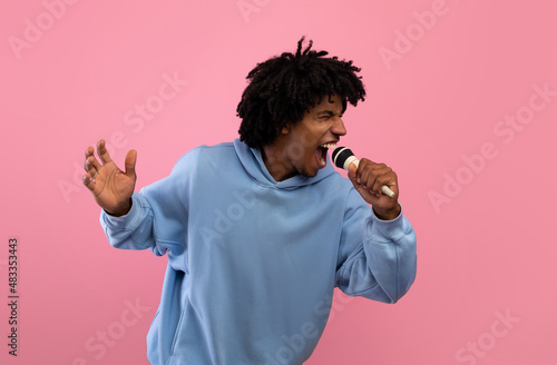 Funky black teenager singing song into microphone  performing karaoke on pink studio background