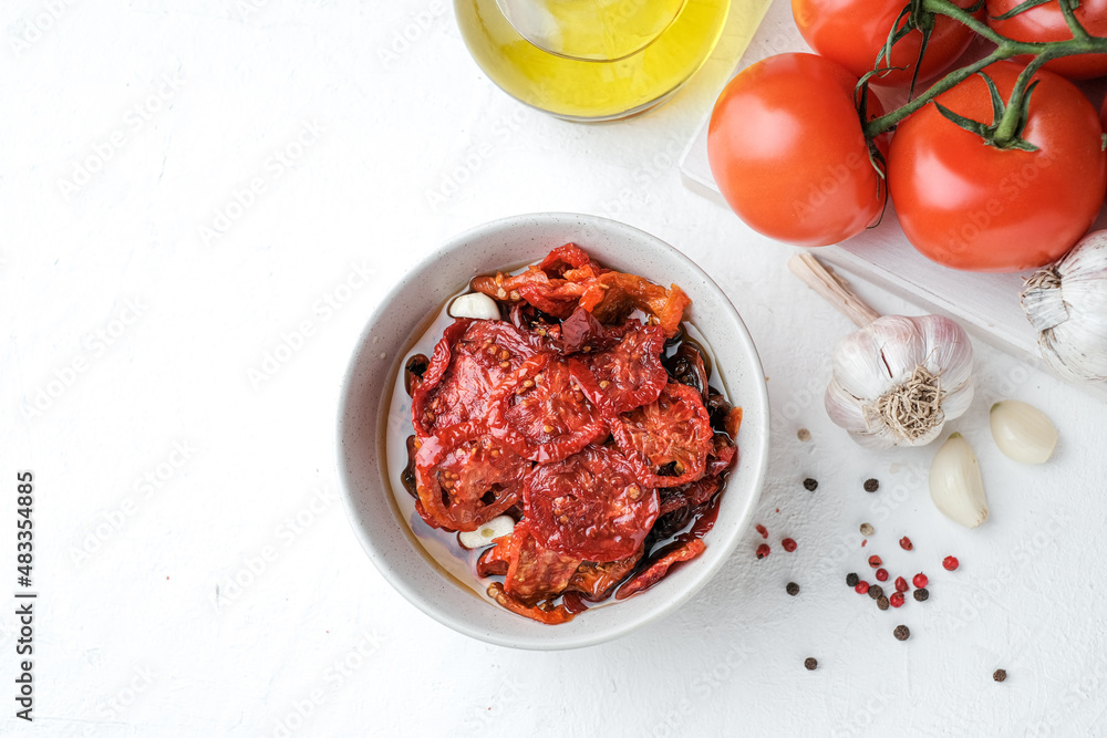 Sun dried tomatoes  on white bowl, white wooden background. Dried tomatoes with olive oil, salt, herbs and garlic recipe.  Top view,  copyspace.